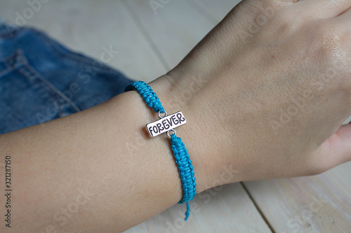 blue bracelet with the word forever on a light wooden background