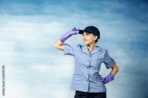 A beautiful young woman in the uniform of a maid and a baseball cap smiling. Isolated on a blue background.