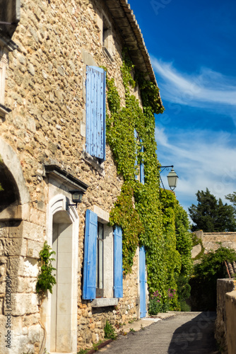 Vertical picture of traditional medieval stone provencal house with blue shutters and ivy on walls in sunny day in Menerbes  one of most beautiful villages of France in heart of Provence. Travel