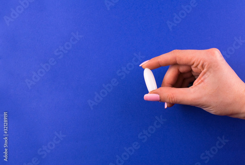  One suppository for anal or vaginal use in a female hand on a blue background. Medical candles. Copy space.