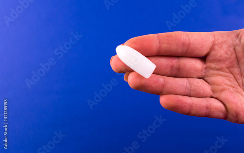  One suppository for anal or vaginal use in a female hand on a blue background. Medical candles. Copy space.