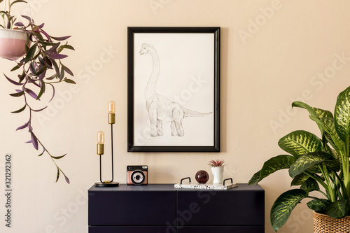 Plakat Stylish interior of living room with black mock up poster frame, plants, table lamp, blue navy commode, photo camera and elegant personal accessories. Beige walls. Modern home staging. Template.