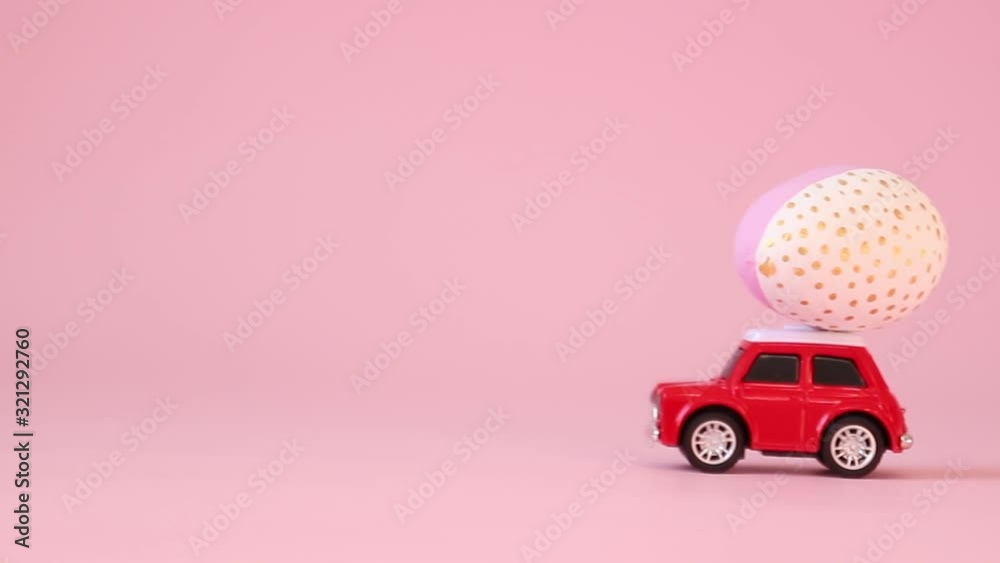 Red toy car model with a golden egg on the hood on a pink background. Gift delivery. Happy easter concept