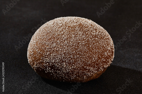 Fresh, palatable baked bun sprinkled with ground coconut against black background with copy space. Rural cuisine or bakery. Close-up