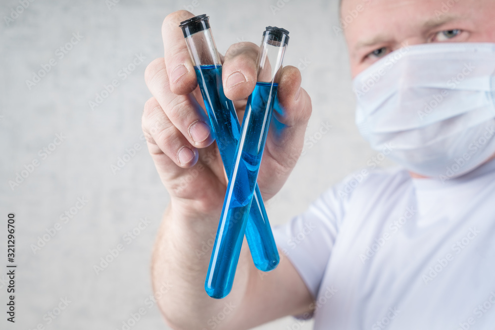 Man in a protective medical mask holds two test tubes with blue liquid. Virus, antivirus. Coronavirus, China. protection, disease, epidemic. Man in a protective medical mask holds two test tubes with blue liquid. Virus, antivirus. Coronavirus, China. protection, disease, epidemic.