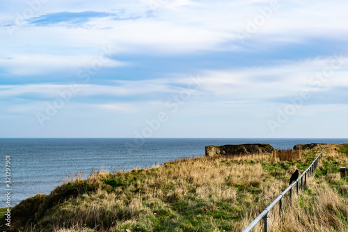 Top of a rough grassy cliff with two Blackbirds perched on a metal railing heading off to the right of the shot.