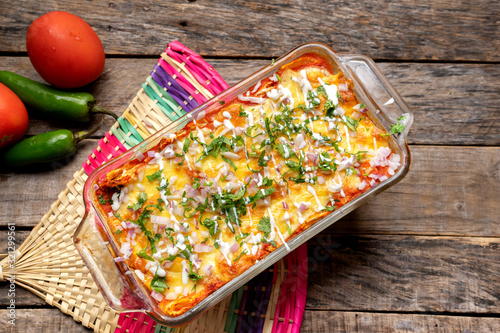 Mexican red baked enchiladas with melted cheese and sour cream on wooden background