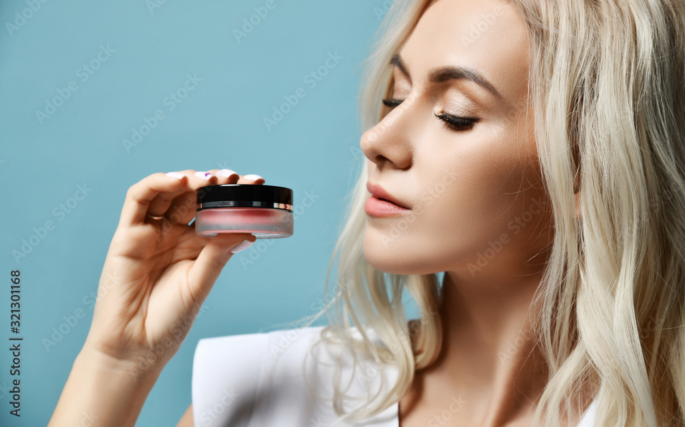 Young beautiful sexy blond woman cosmetologist in white medical uniform is holding looking at skin cream small jar Young beautiful sexy blond woman cosmetologist in white medical uniform is holding looking at skin cream small jar