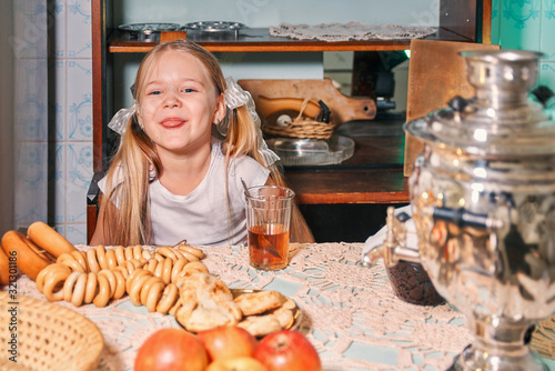 little girl drinks tea in the evening. on the table are buns, bagels, cookies and samovar