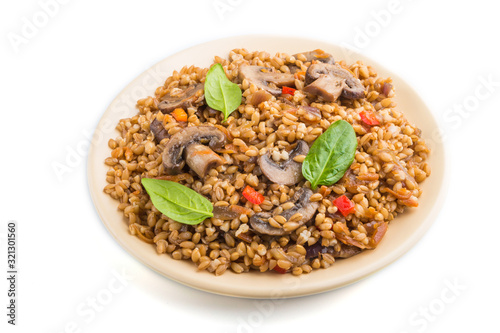 Spelt (dinkel wheat) porridge with vegetables and mushrooms on ceramic plate isolated on white background. Side view, close up.
