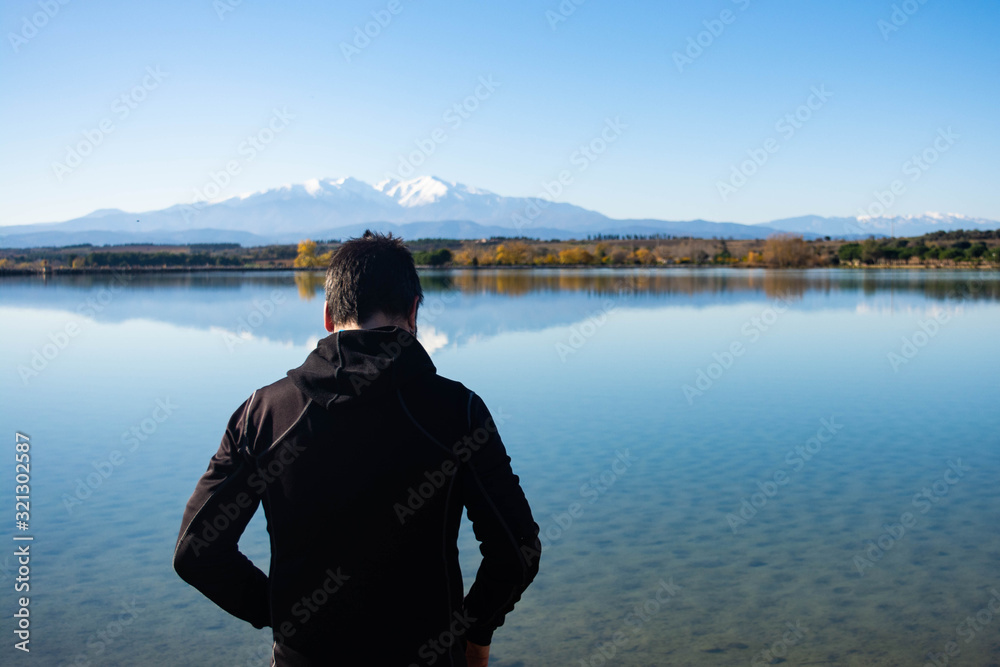 Adventurous man observes a lake with mountains on the horizon