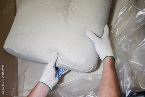 Assembling furniture for workers for home, office and hotel. Repair and renovation of interior indoors. Hands of a man in white gloves unpack pillows of a new sofa.