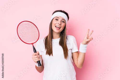 Young caucasian woman playing badminton isolated joyful and carefree showing a peace symbol with fingers. © Asier