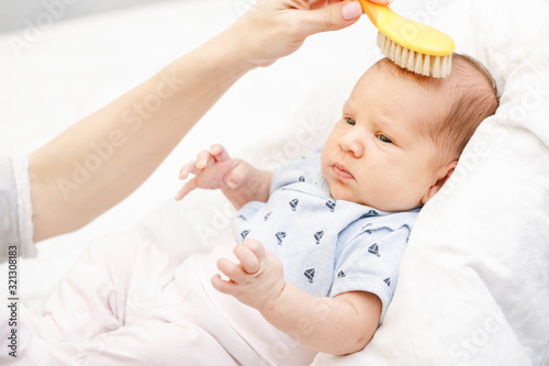 Mother brushing hair of newborn baby with soft brush