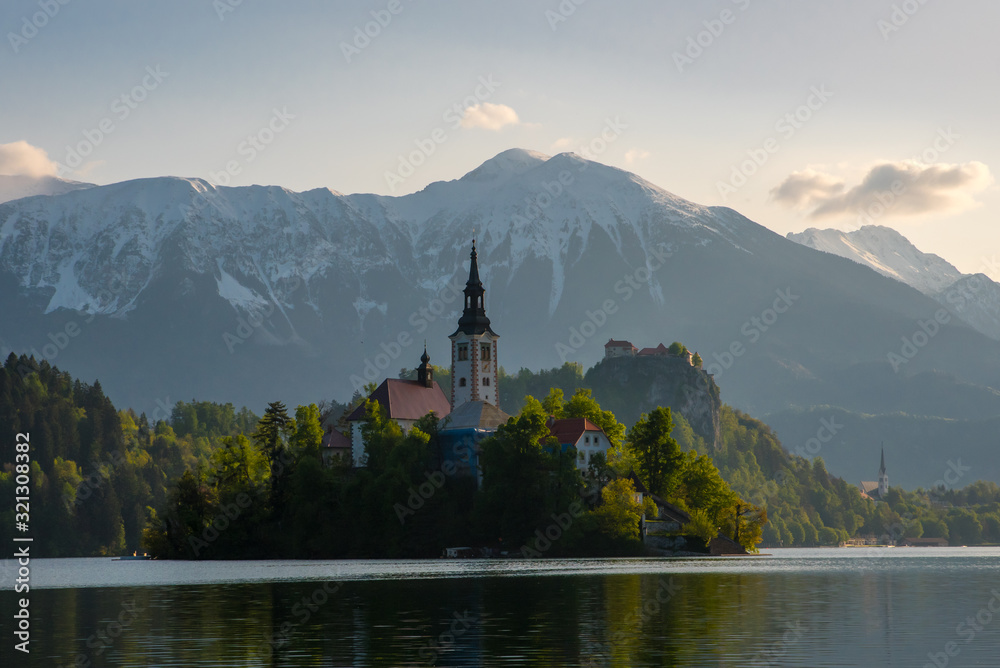 The Pilgrimage Church of the Assumption of Maria on the island on Lake Bled, Slovenia with the surroundings mountains and the Bled castle in the background, at dawn