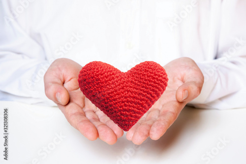 Red heart in the hands of a young Caucasian type man on a light background. Valentine's day concept. Copy space for your text.