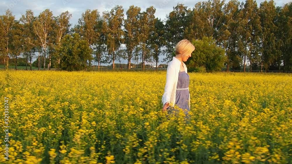 an attractive young blonde woman walks through a field of rapeseed, smiling and spinning merrily. Slow motion