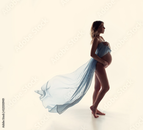Pregnancy woman open tummy naked body skin. Photoshoot of a pregnant girl with flying blue cloth. Health concept awaiting birth tenderness happiness of motherhood. Femininity is freedom. Waiting boy