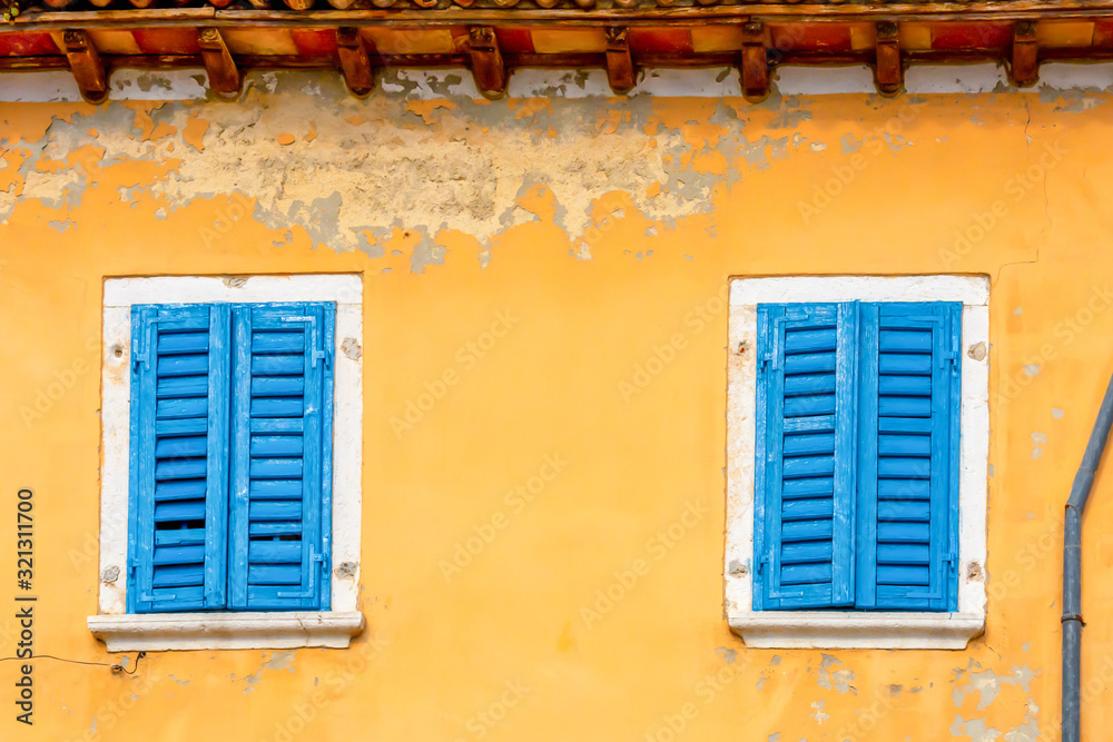 Facade of an old yellow house with blue shutters. Croatia