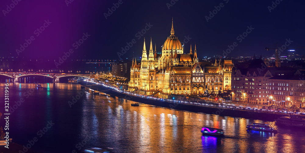 Colorful sunset over Budapest. Wonderful evening cityscape. Night view of the illuminated building of the Hungarian parliament over Danube river with reflected. Popular touristic locations