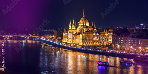 Colorful sunset over Budapest. Wonderful evening cityscape. Night view of the illuminated building of the Hungarian parliament over Danube river with reflected. Popular touristic locations