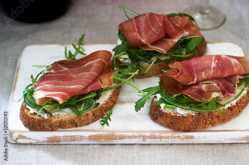 Traditional italian appetizer bruschetta of toasted bread with cottage cheese, arugula and prosciutto.