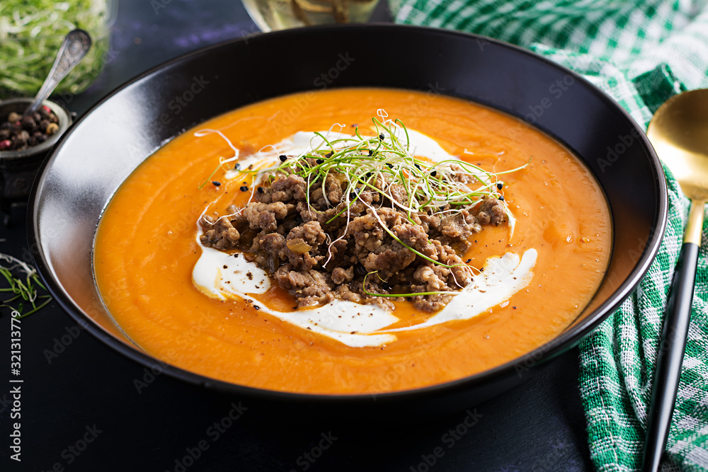 Delicious cream of pumpkin soup with roasted forcemeat made of beef minced meat in a bowl on a dark table. Thanksgiving Day.