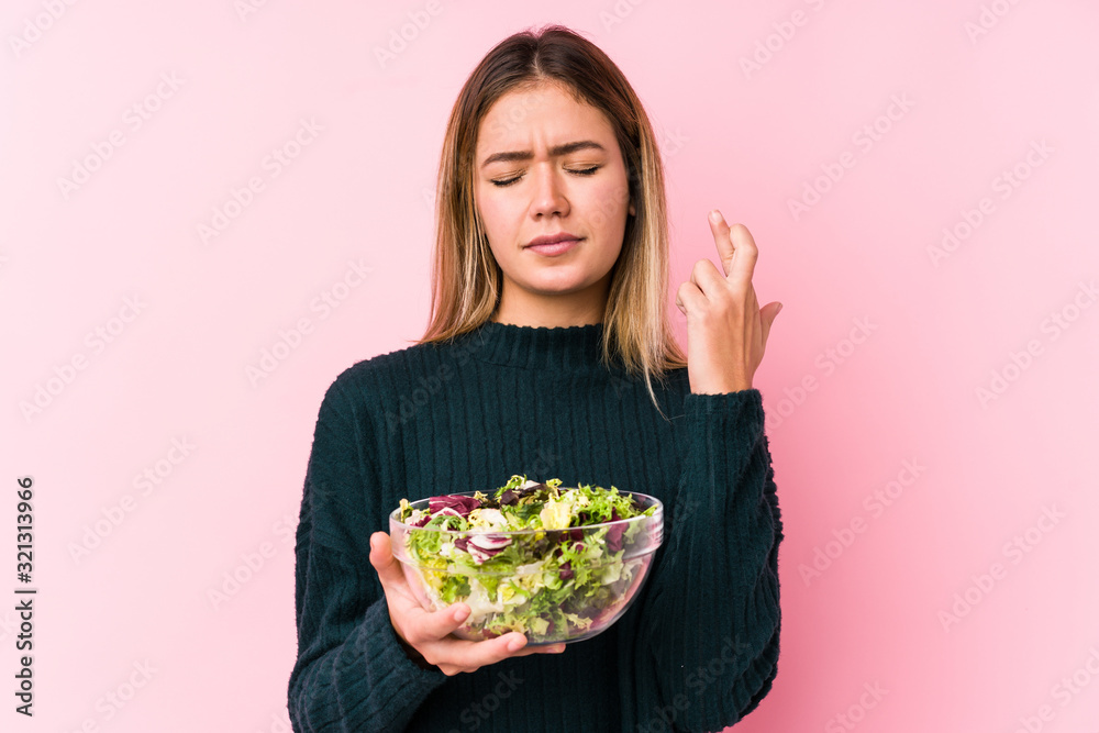 Young caucasian woman holding a salad isolated crossing fingers for having luck
