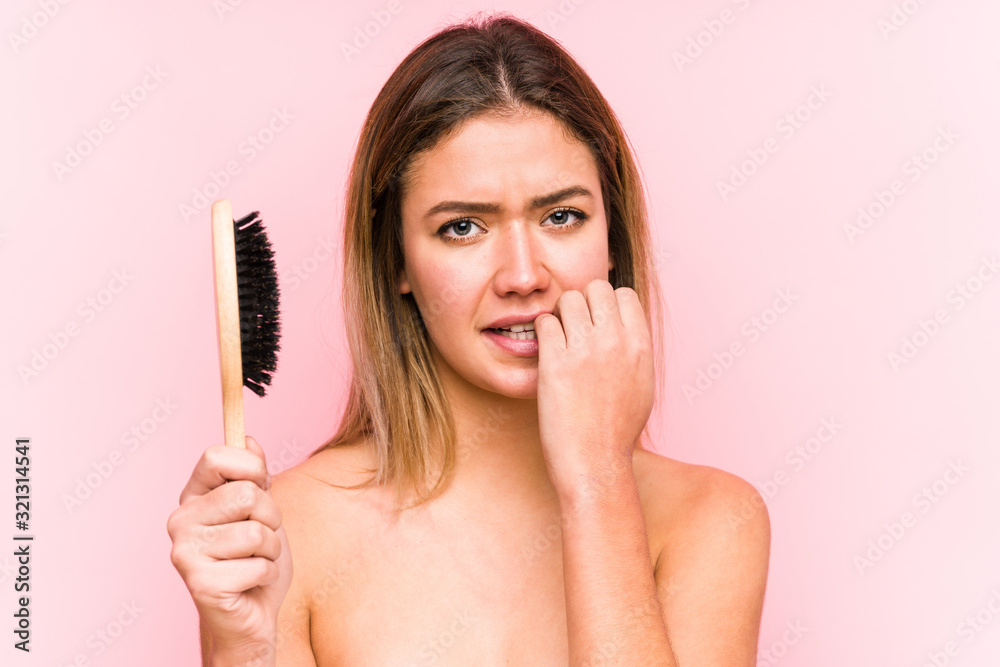 Young caucasian woman holding a hairbrush isolated biting fingernails, nervous and very anxious. Young caucasian woman holding a hairbrush isolated biting fingernails, nervous and very anxious.