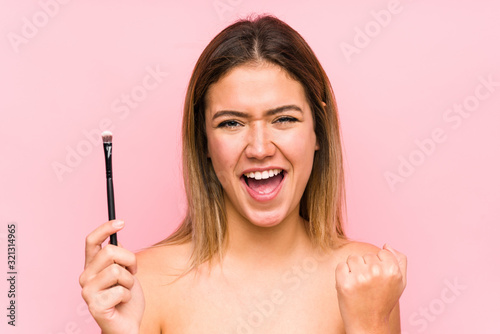 Young caucasian woman holding a eyebrush isolated cheering carefree and excited. Victory concept. photo
