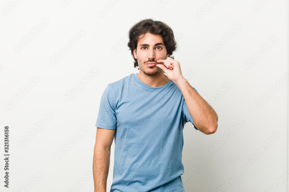 Young handsome man against a white background with fingers on lips keeping a secret. Young handsome man against a white background with fingers on lips keeping a secret.