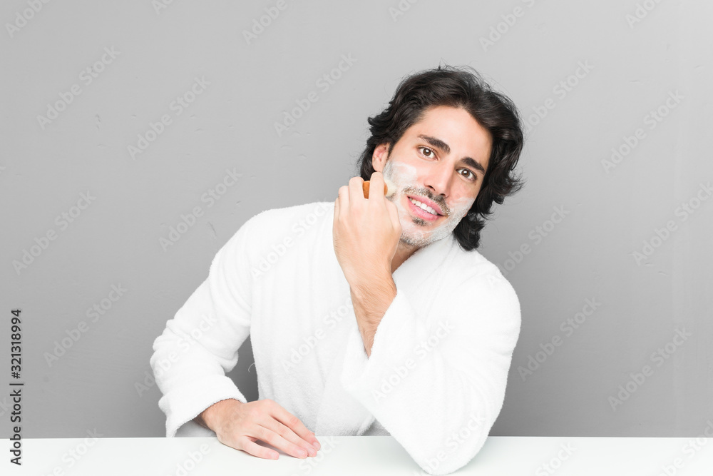 Young caucasian man shaving his beard isolated on a grey background Young caucasian man shaving his beard isolated on a grey background