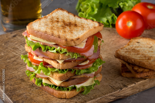 Delicious sandwich with ham, cheese, tomatoes, lettuce. High club sandwich with toast. close up of fresh sandwich with ham, bacon,tomatoes,cheese and lettuce On a wooden board. Sandwich bread tomato, 