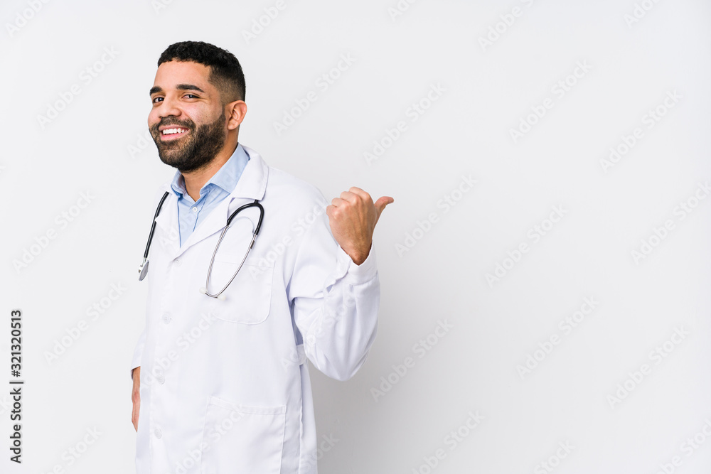 Young arabian doctor man isolated points with thumb finger away, laughing and carefree.