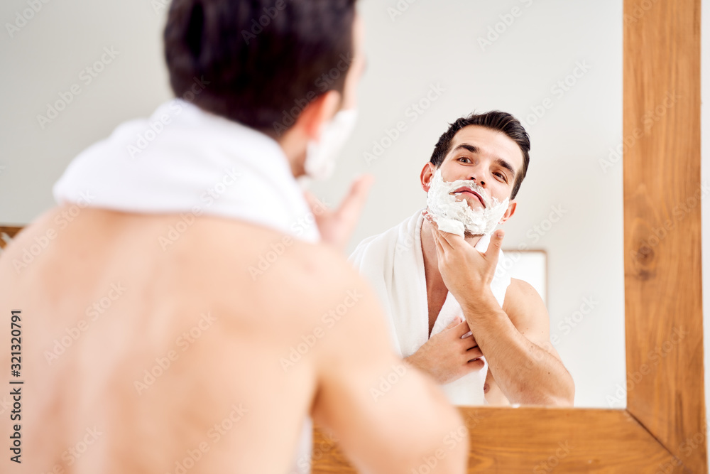 Brunet male with foam on beard near mirror in morning