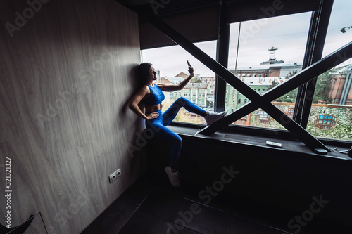 Pretty girl sitting on the window sill with smartphone in hands.