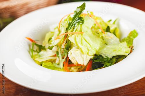 Fresh mixed green salad with carrot on white plate.