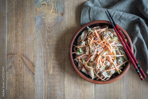 Spicy salad with Korean carrots, meat and vegetables in a brown clay plate on a wooden background