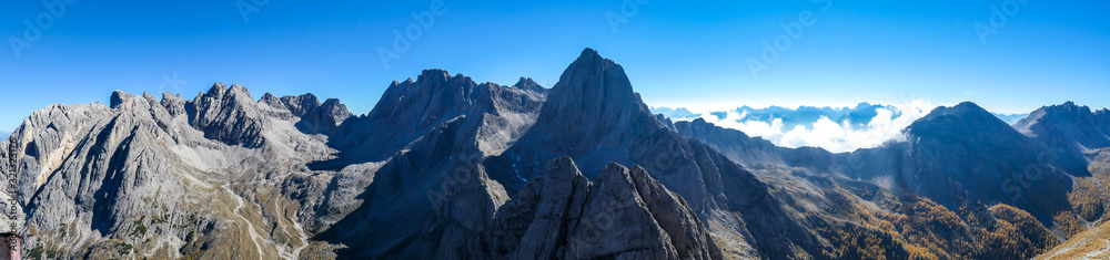 A panoramic view on Lienz Dolomites, Austria from the top of Grosse Gamswiesenspitze, bathing in the morning sun. The valley is shrouded in fog. High mountain climbing. Freedom and solitude