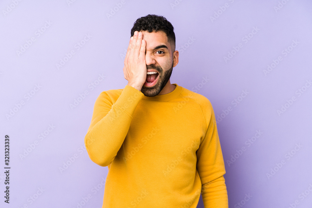 Young mixed race arabic man isolated having fun covering half of face with palm. Young mixed race arabic man isolated having fun covering half of face with palm.