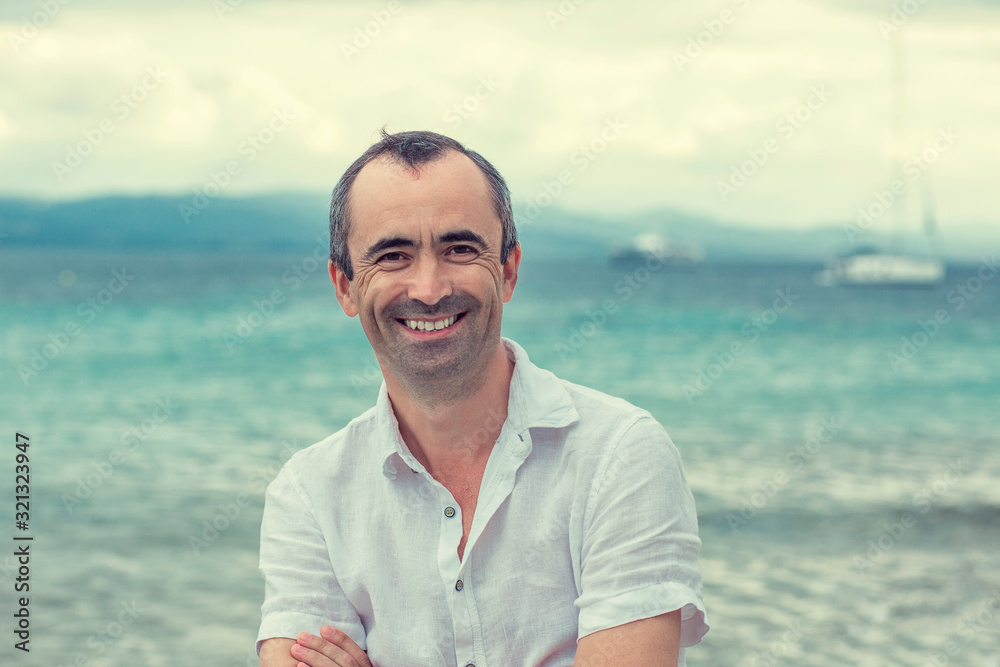 Smiling man with crossed arms by the sea, toothy smile middle ag