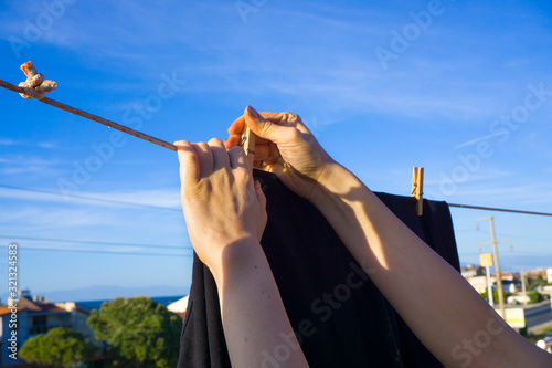 Female hand hanging clothes with wooden pegs to clothes line. Lots of clothes on blue sky background.