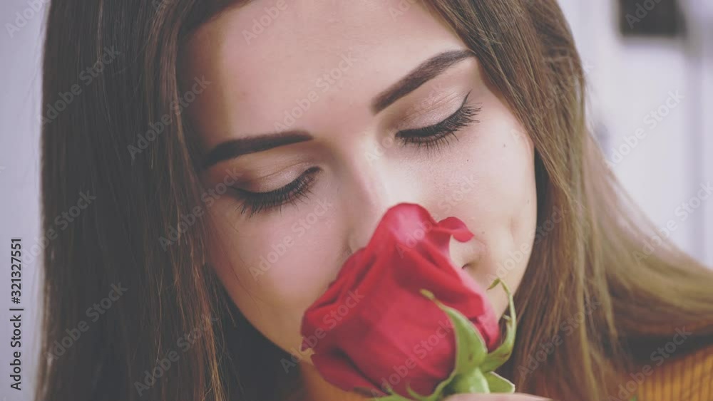 Gorgeous brunette girl is smelling a rose in a cafe. Close up. Crop. Copy space. 4K.