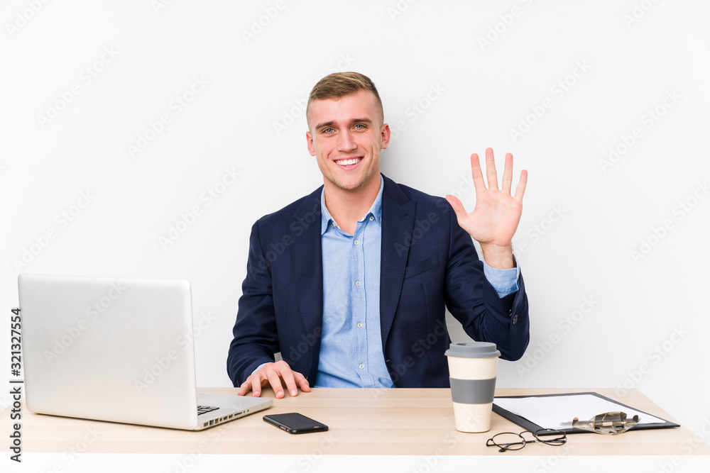 Young business man with a laptop smiling cheerful showing number five with fingers.