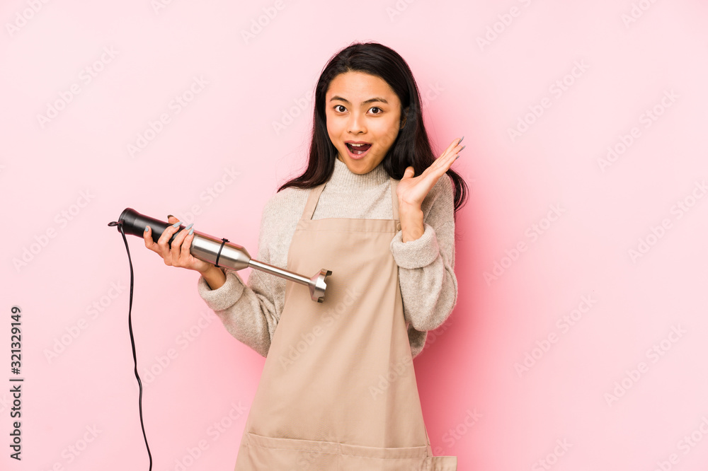 Young chinese woman holding a mixer isolated screaming very angry and aggressive. Young chinese woman holding a mixer isolated screaming very angry and aggressive.