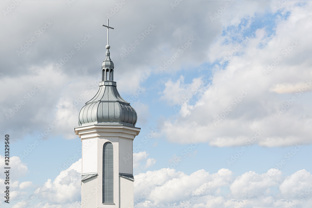 View of the dome and bell tower of a modern Catholic church against a blue sky with clouds. Concept architecture, easter, religion