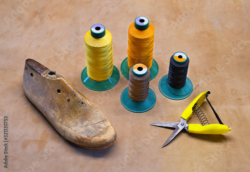 Boot maker tools. Bootmaker equipment on leather underlay. Sewing things with boot-tree. Sewing thread with the shoelast. Shoetree with hand shears and coloured sewing thread. Shoemaker's scissors