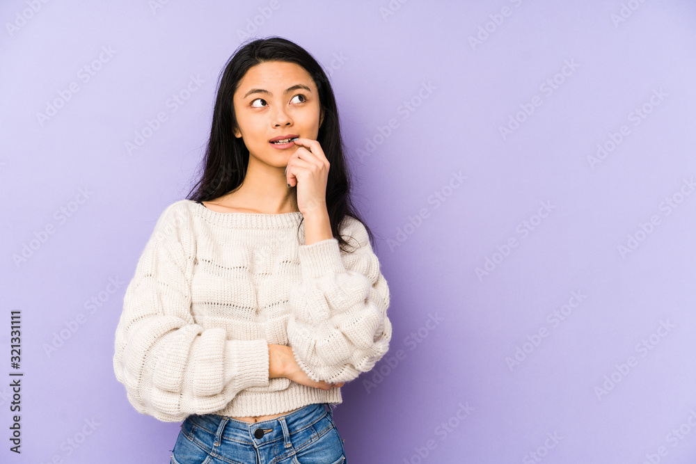 Young chinese woman isolated on a purple background relaxed thinking about something looking at a copy space. Young chinese woman isolated on a purple background relaxed thinking about something looking at a copy space.