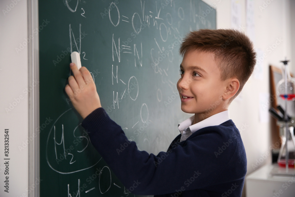 Schoolboy writing chemical formulas on chalkboard in classroom