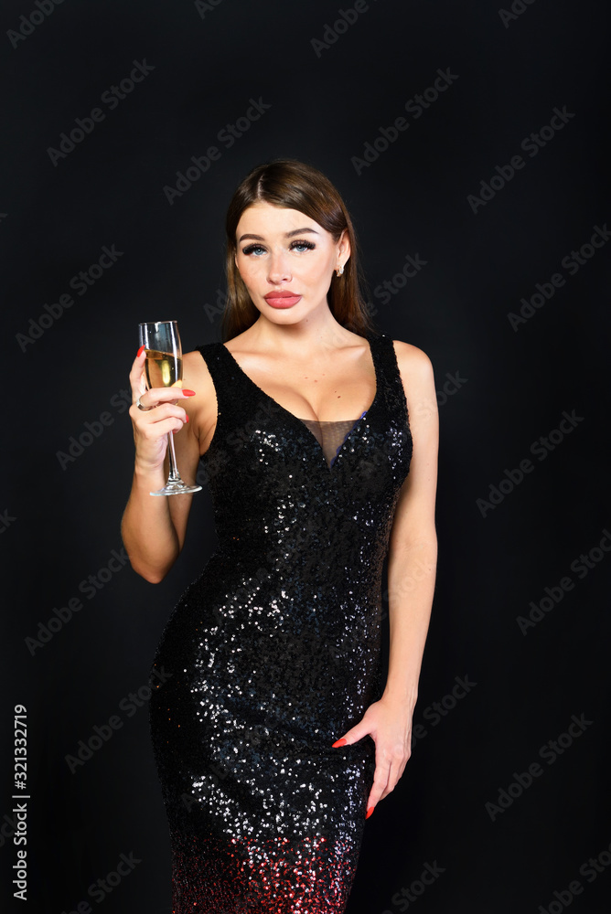 Young sexy woman in evening dress holds a glass of champagne against a black wall. Young sexy woman in evening dress holds a glass of champagne against a black wall.